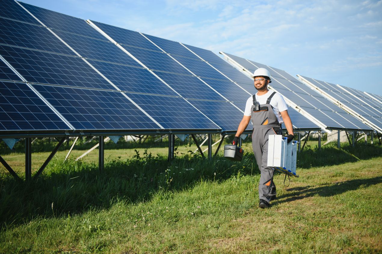 Ein Solartechniker mit Werkzeug geht entlang einer großen Photovoltaikanlage – der PV Großhandel liefert die passenden Komponenten für reibungslose Installationen.