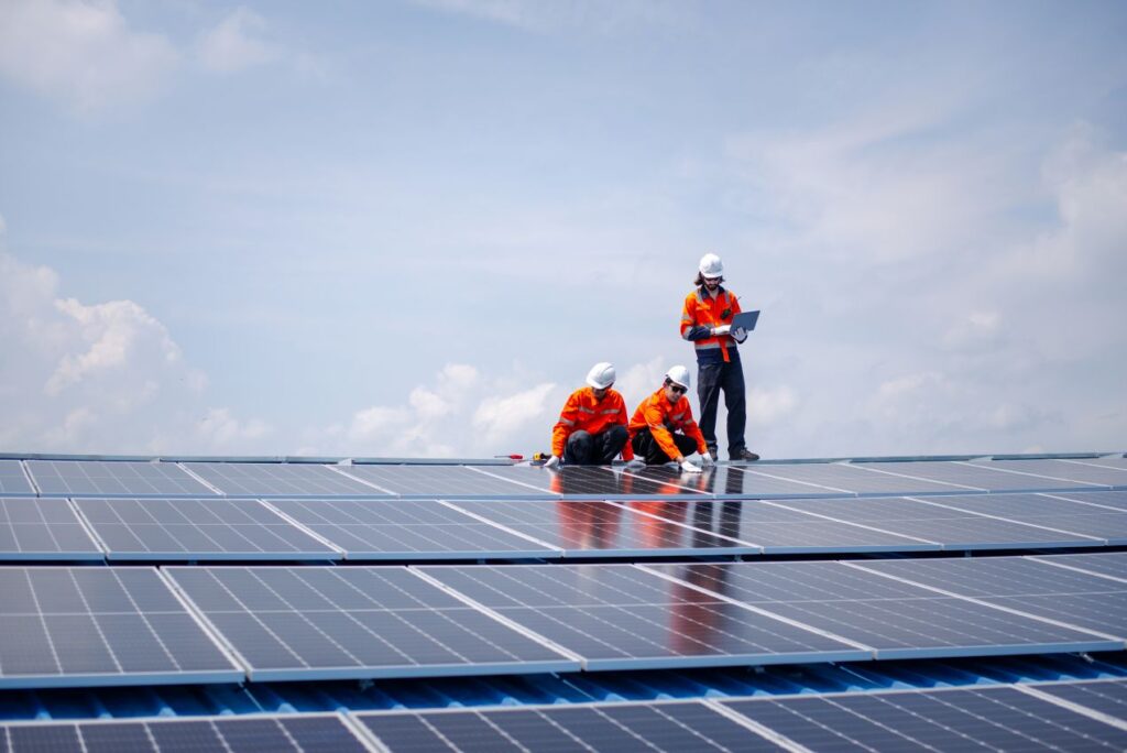 Drei Solarteure installieren Solarmodule auf einem Dach – der PV Großhandel liefert hochwertige Komponenten für reibungslose Montage.