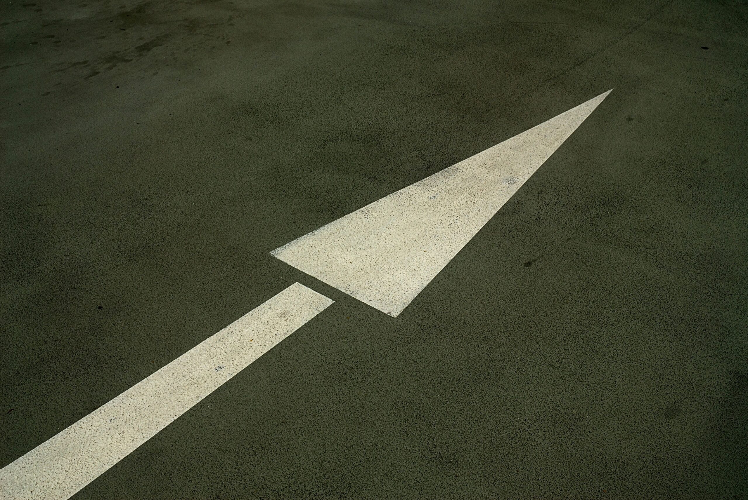 Weiße Richtungspfeil-Markierung auf dunklem Asphalt als Symbol für Regelvorgaben bei Parkflächenmarkierung
